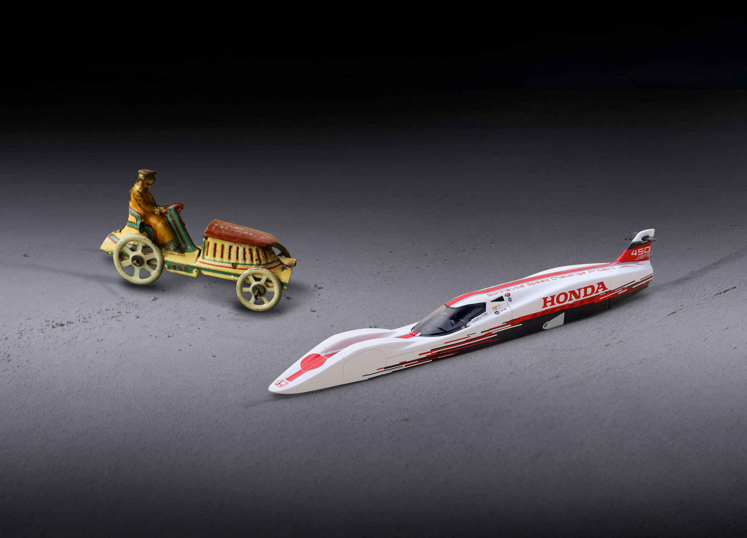 A tin toy racer from the 1900s beside a modern Honda Bonneville streamliner model